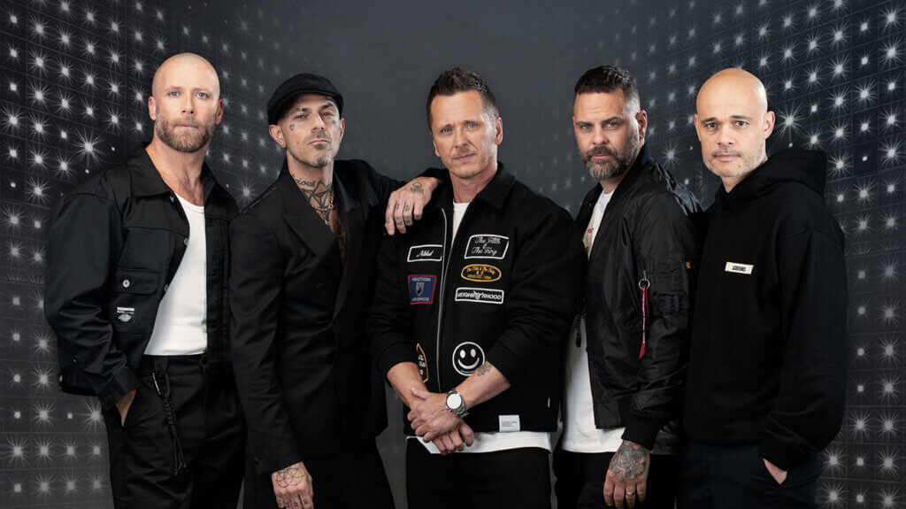 Five band members in black jackets standing closely together, posing for a photo.