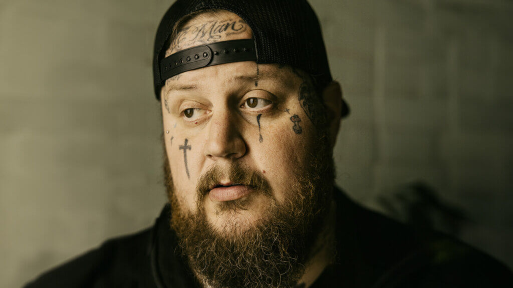 The singer Jelly Roll, featuring a beard and tattoos, gazes at the camera.