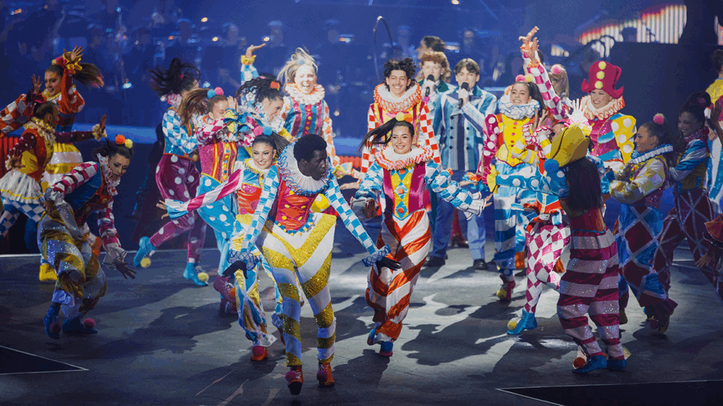 A lively group of school students performs on stage in front of a large audience at the Victorian State Schools Spectacular.