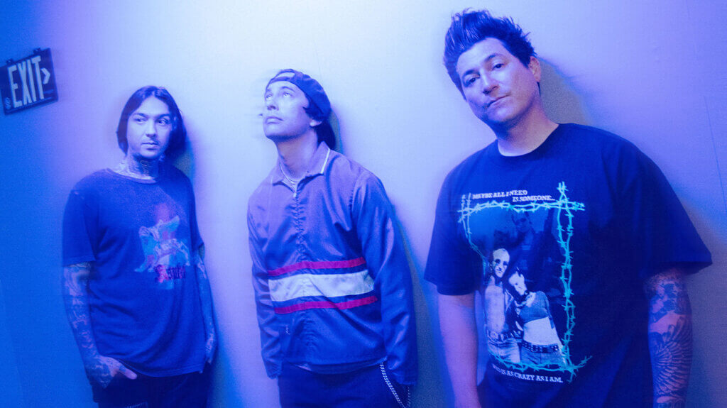 Band members of Pierce The Veil pose in front of a bright blue wall.