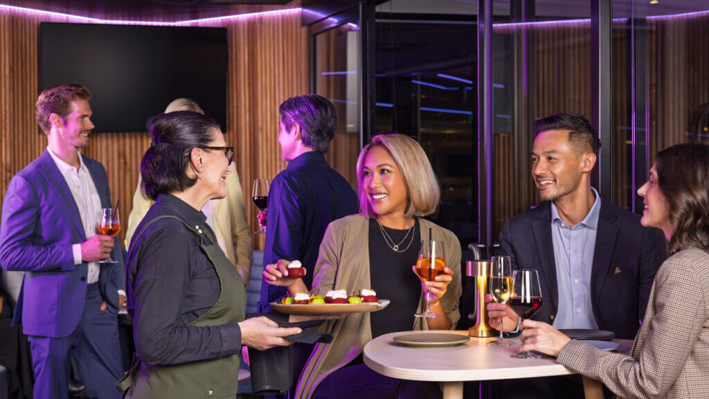 A group of people enjoying food and drink at a corporate event in a John Cain Arena suite.