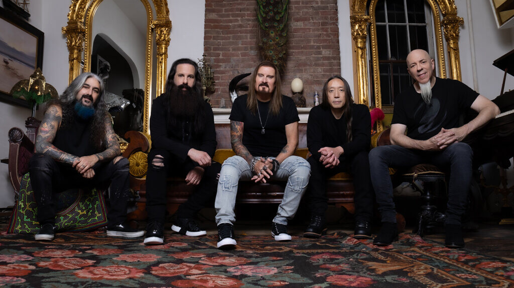 Dream Theater band members seated on a rug in front of an ornate gold mirror.