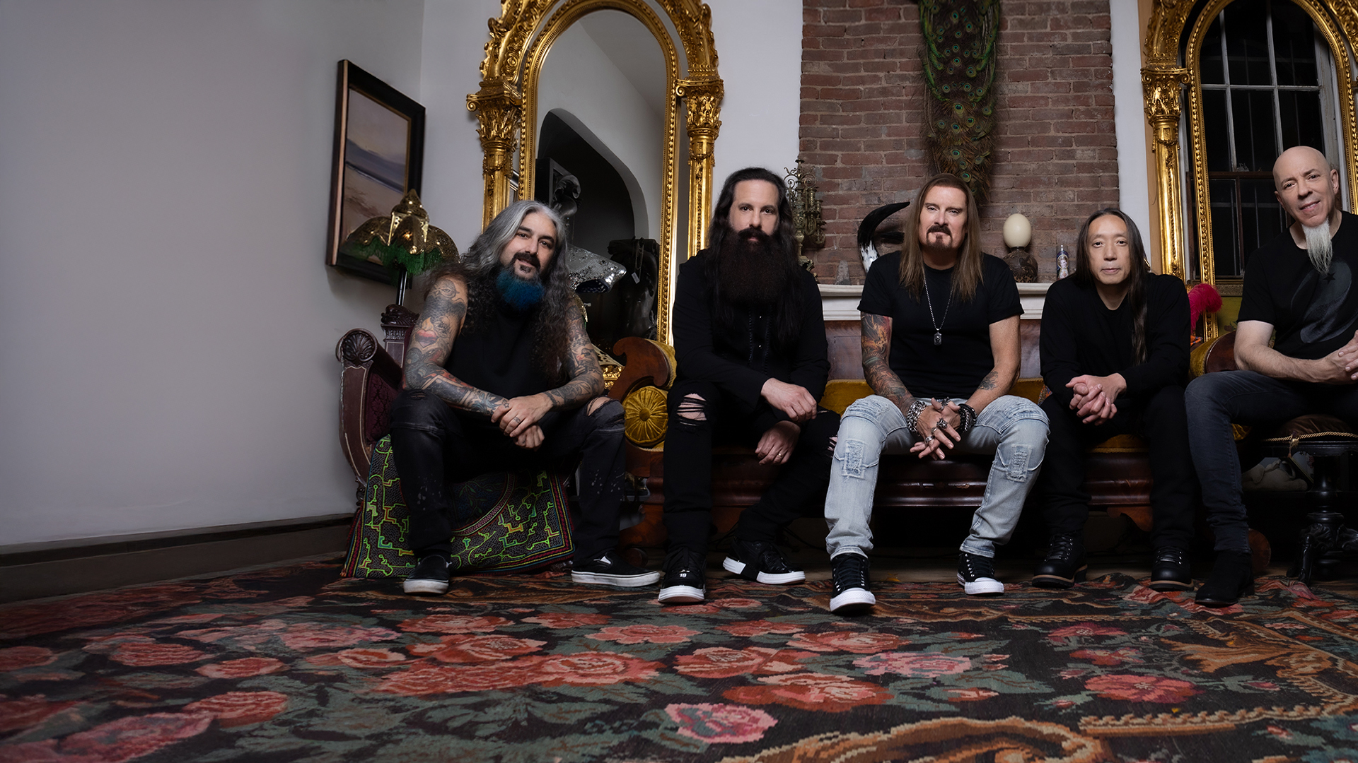 Dream Theater band members seated on a rug in front of an ornate gold mirror.
