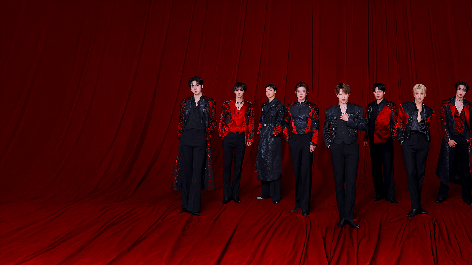 ATEEZ band members dressed in suits posing against a red draped background.