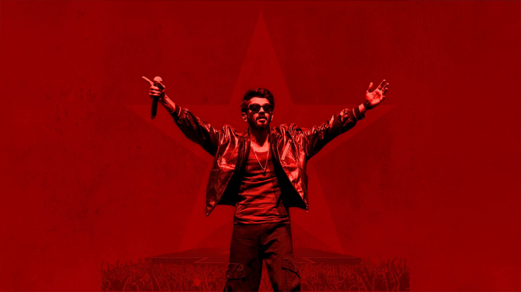 Singer Anirudh with microphone in hand and arms in the air against a red background.