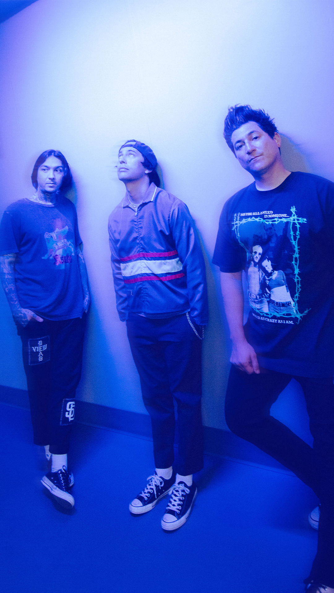 Band members of Pierce The Veil pose in front of a bright blue wall.
