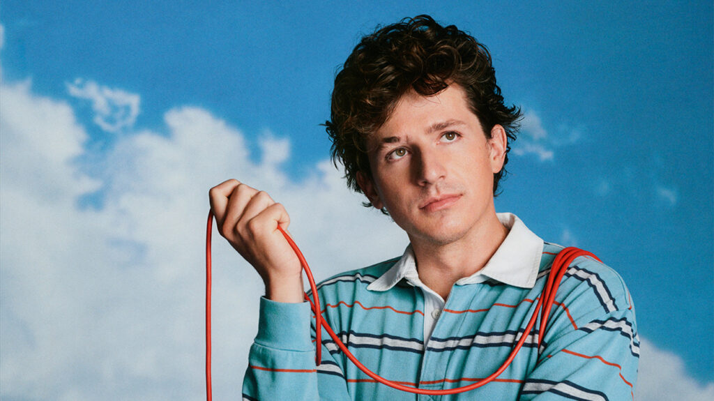Charlie Puth holds a red cord against a clear blue sky.