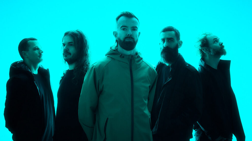 Karnivool band members posing together in front of a neon blue background.