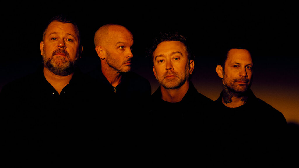 Rise Against band members band pose together in front of a solid black background.