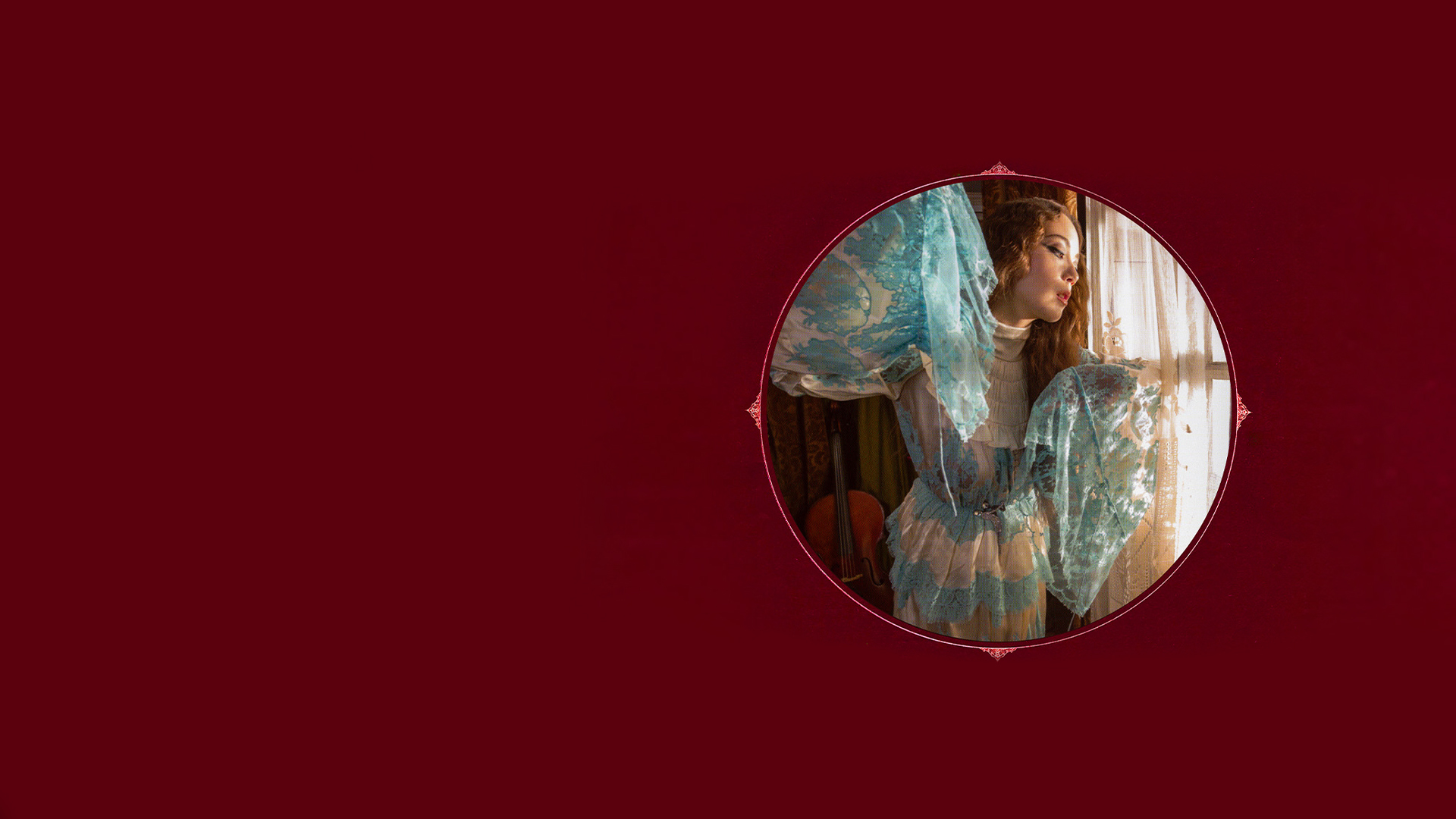 Laufey in a blue dress stands gracefully in front of a large window.