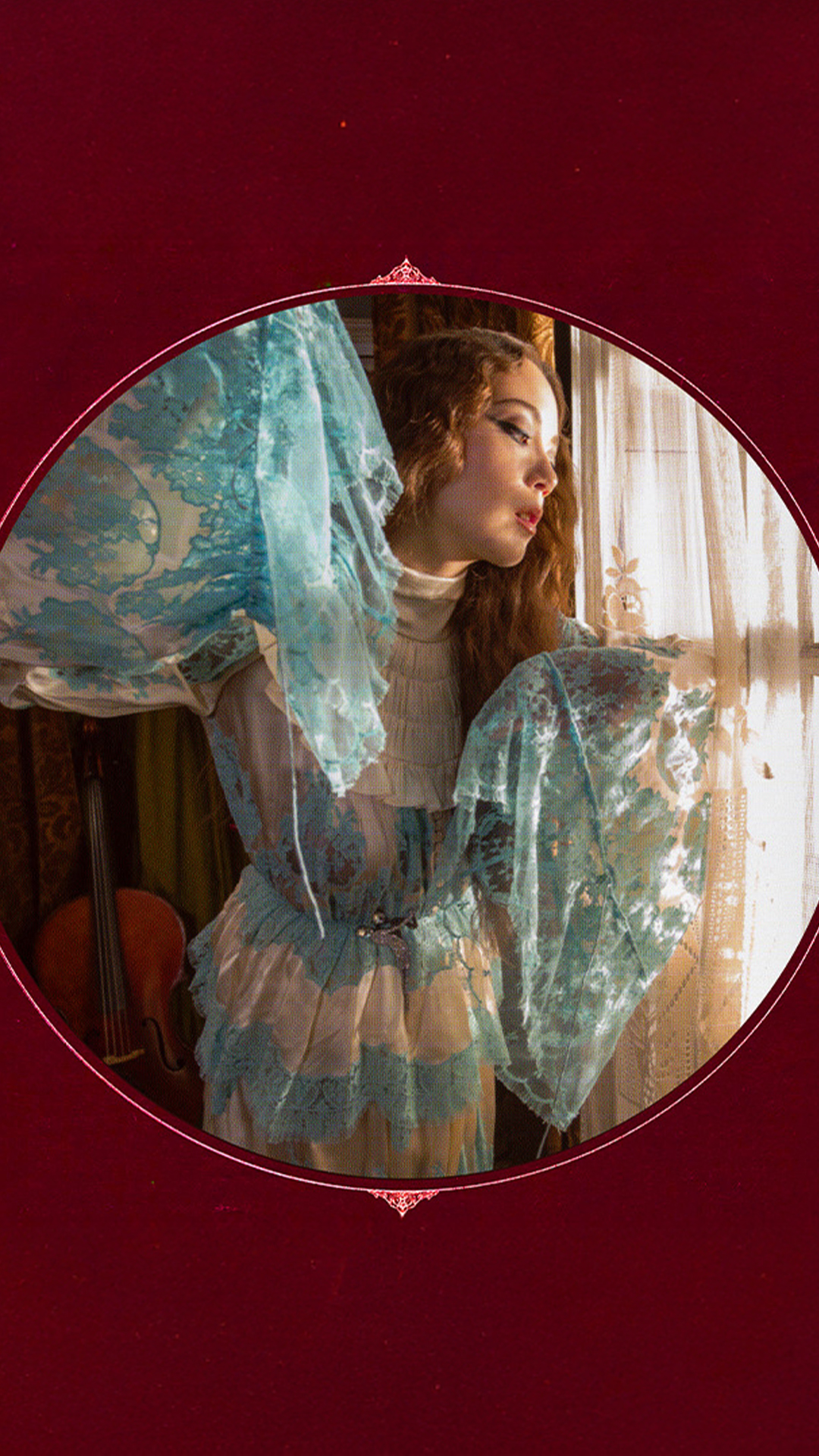 Laufey in a blue dress stands gracefully in front of a large window.