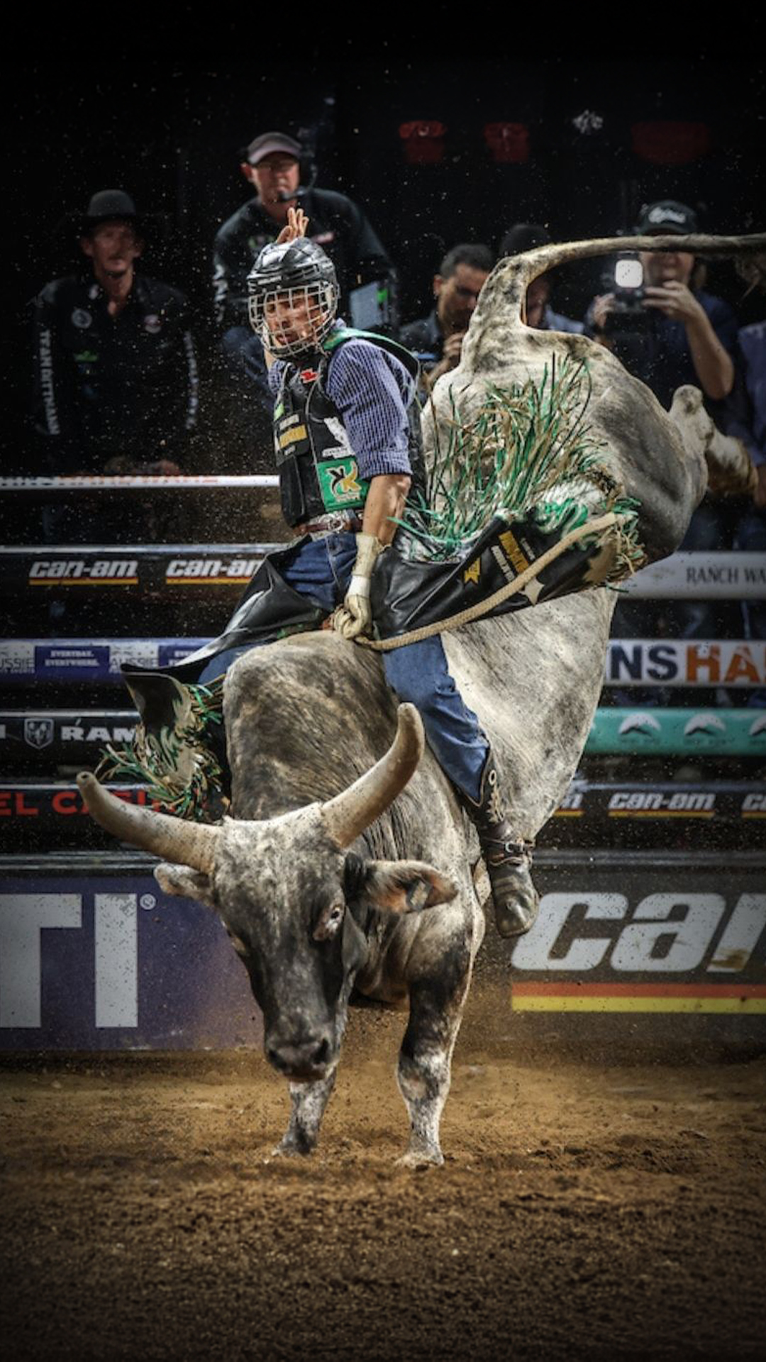 A man in a cowboy hat rides a bucking bull in a rodeo arena, surrounded by cheering spectators.
