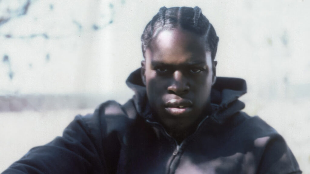 Daniel Caesar with dreadlocks gazes directly at the camera.
