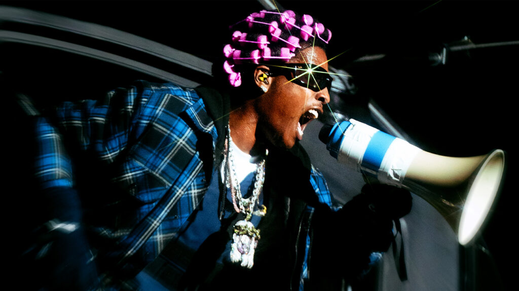A man wearing a pink hat holds a megaphone, speaking passionately to a crowd.
