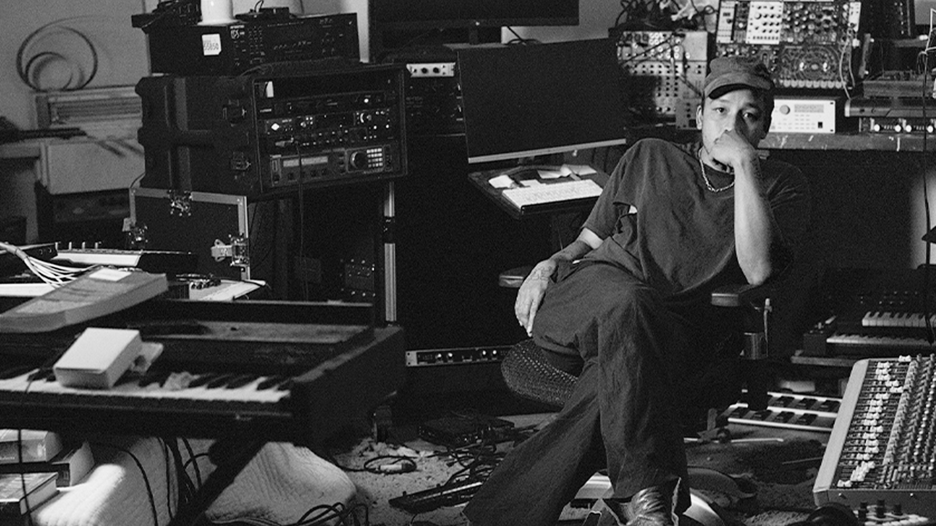 Dijon seated in a room filled with various electronic and musical equipment.
