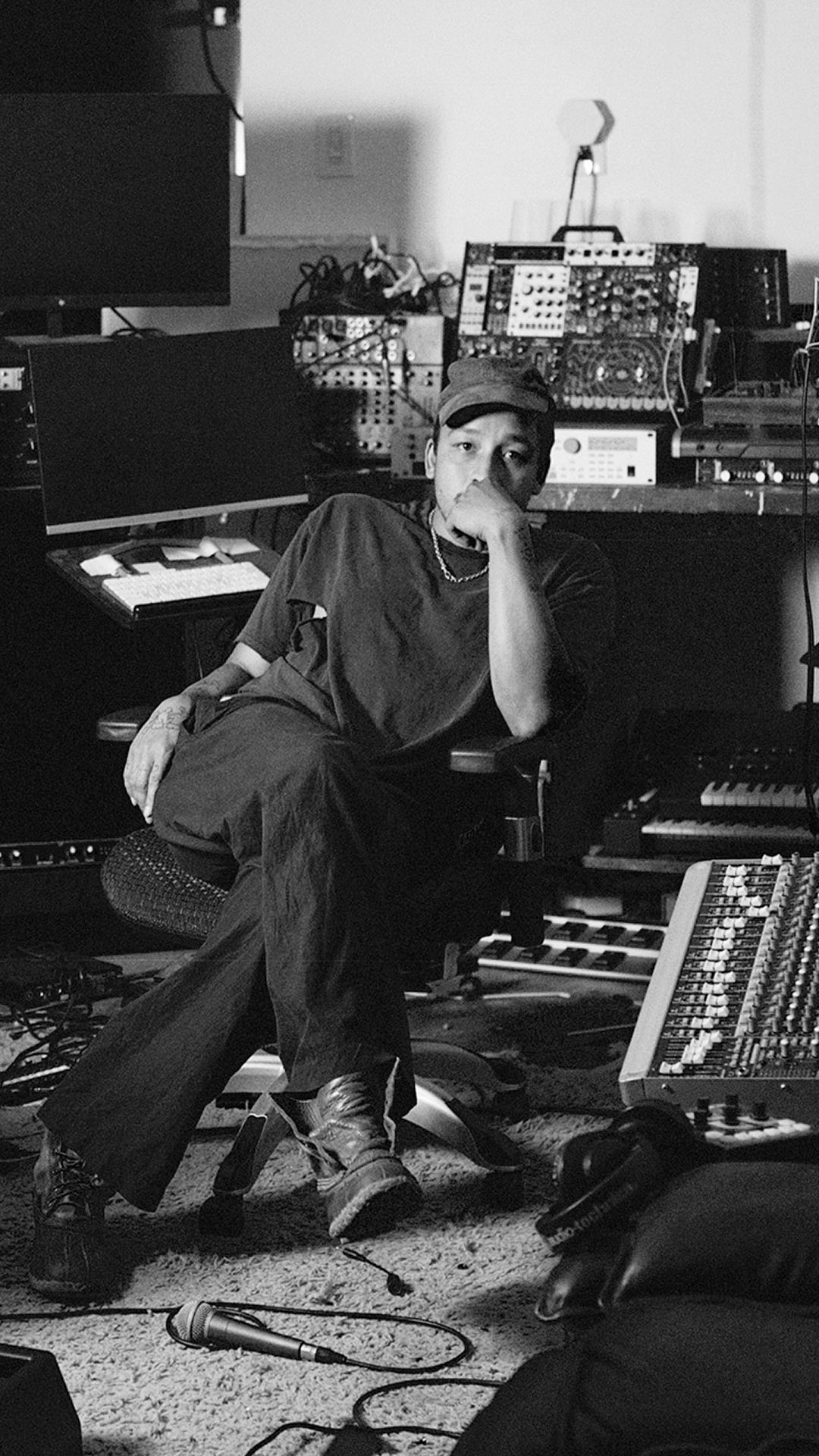 Dijon seated in a room filled with various electronic and musical equipment.