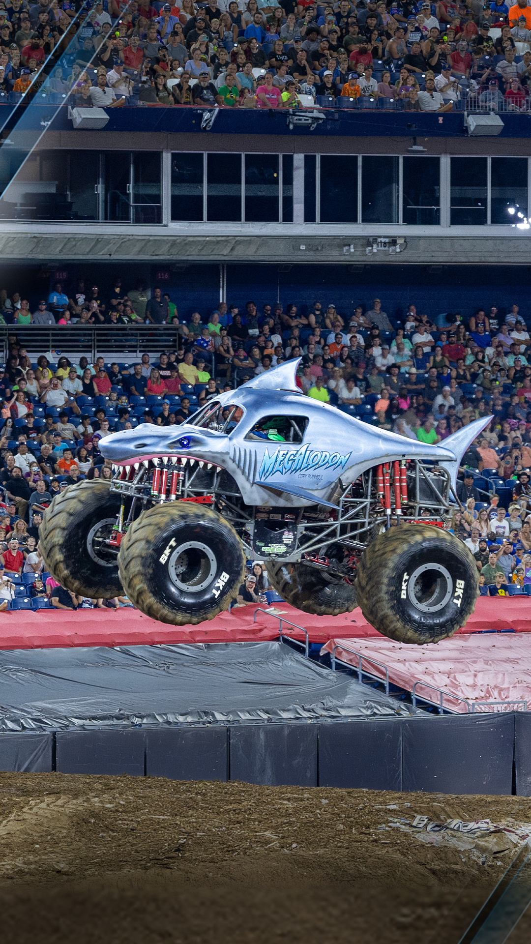 A monster truck soars above a cheering crowd during a motorsport event.