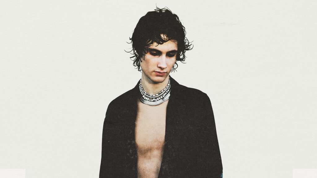 A shirtless Sombr wearing a necklace, posing against a white background.