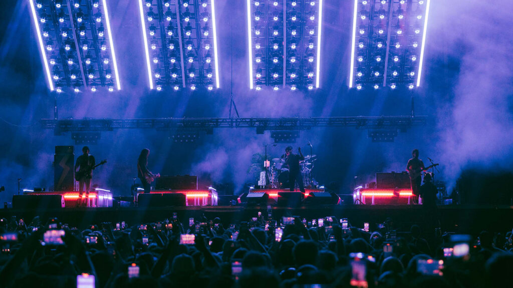 The Strokes performing on stage, surrounded by colourful lights and smoke.