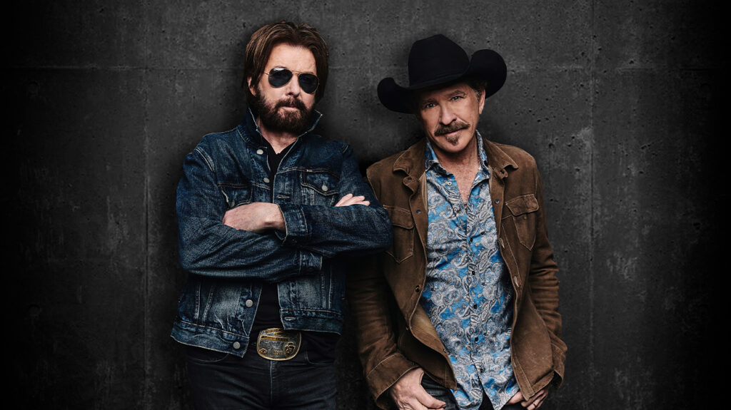 Two men wearing cowboy hats stand side by side, smiling at the camera in a casual outdoor setting.