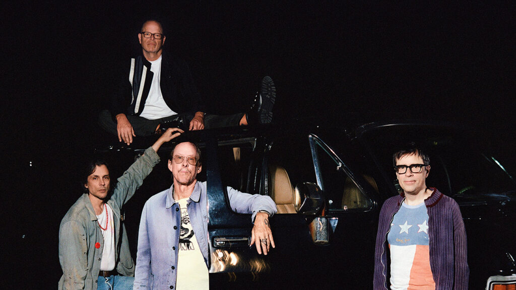 Weezer band members posing next to and on top of a car.